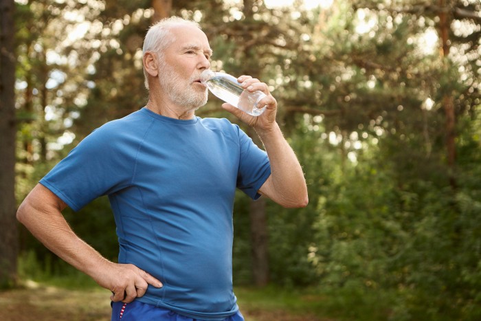portrait-attractive-active-male-pensioner-with-bald-head-stubble-refreshing-himself-after-jogging-outdoors-standing-against-pine-forest-holding-bottle-drinking-water